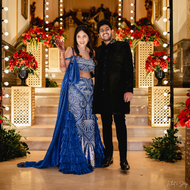 Glamorous Indian couple in traditional attire posing during their wedding reception. The bride is in blue and the groom is in black.
