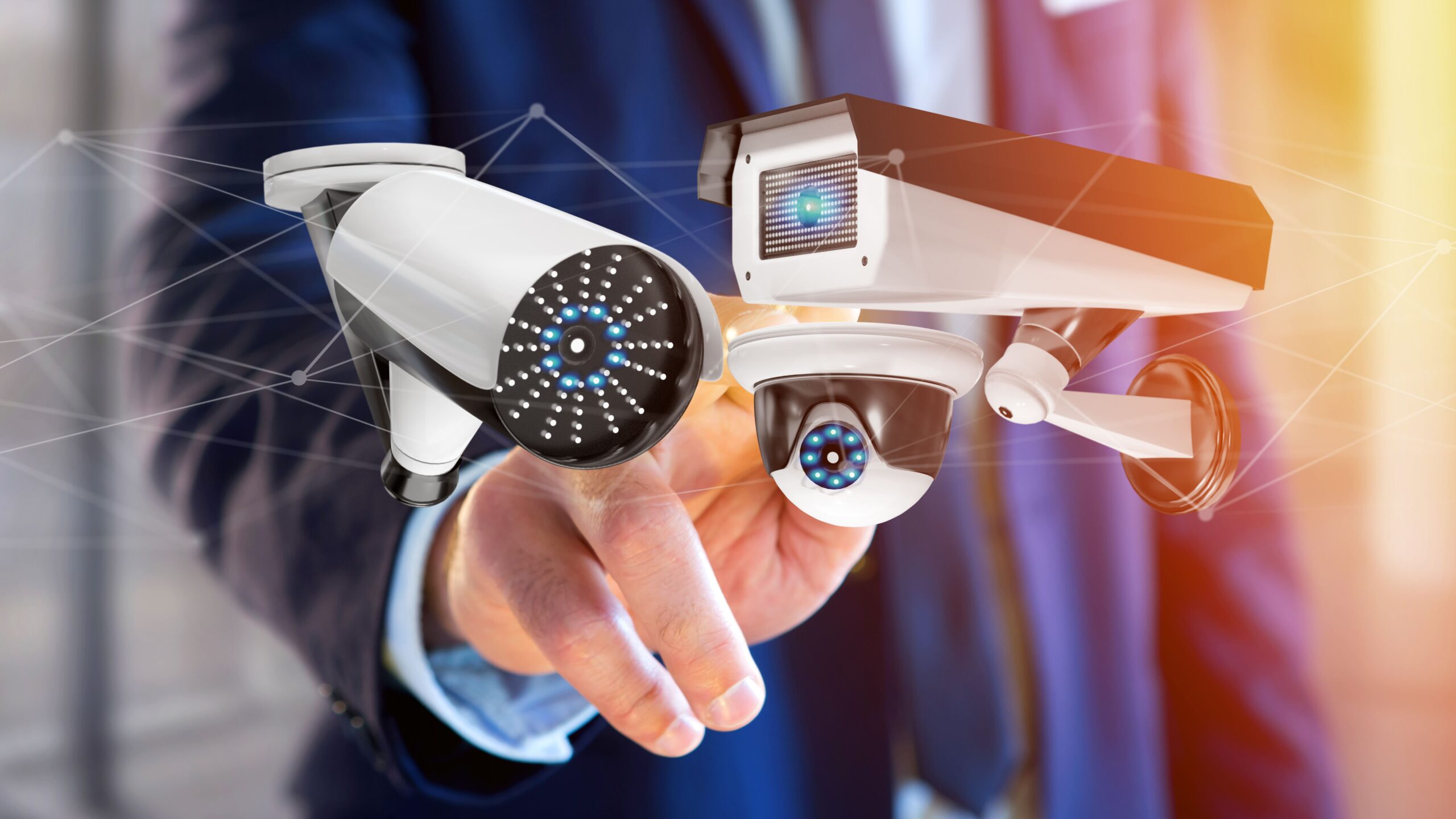 A hand in a suit points directly at the viewer, surrounded by multiple security cameras of different types aimed at the fingertip, with digital network lines in the background, symbolizing surveillance and privacy concerns.