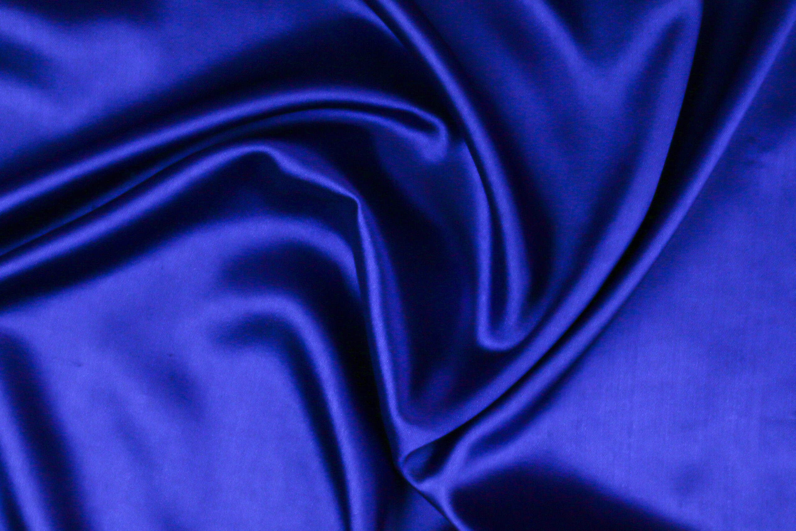 Close-up of smooth, royal blue satin fabric with soft folds and a glossy, reflective surface.